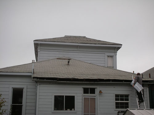 Noel approaches the roof with bundle of shingles